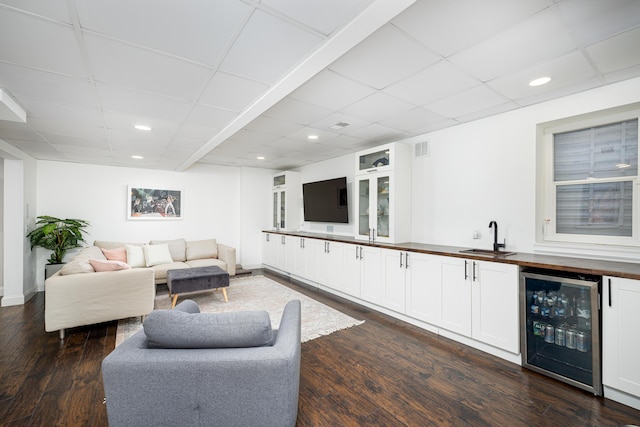 living room featuring beverage cooler, dark wood finished floors, a drop ceiling, wet bar, and recessed lighting