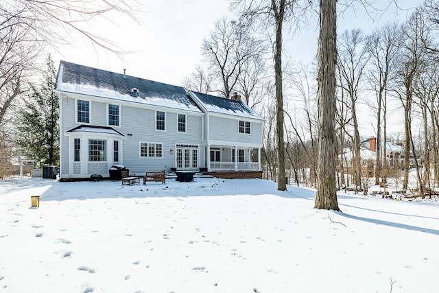 snow covered house featuring a chimney and central AC