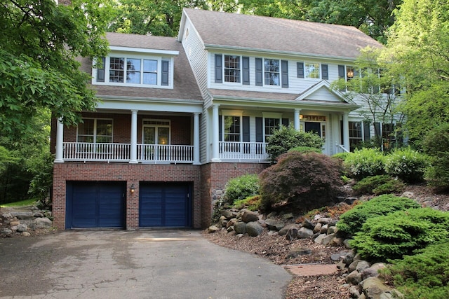 colonial-style house with brick siding, driveway, an attached garage, and roof with shingles