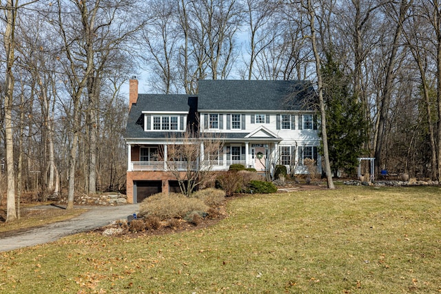 colonial home featuring aphalt driveway, a front yard, covered porch, a chimney, and a garage