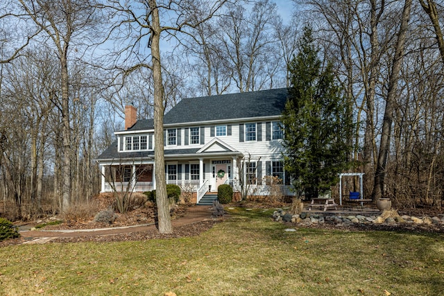 colonial inspired home featuring a front lawn, covered porch, a chimney, and a shingled roof