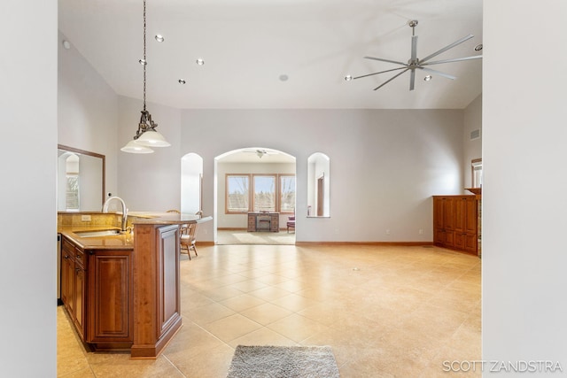 kitchen featuring arched walkways, pendant lighting, open floor plan, a sink, and ceiling fan