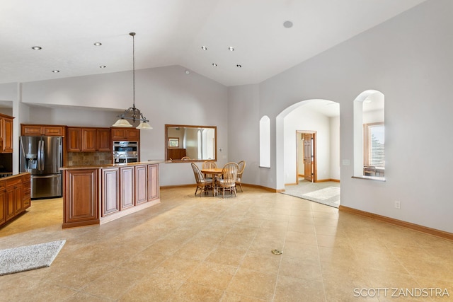 kitchen featuring high vaulted ceiling, stainless steel refrigerator with ice dispenser, tasteful backsplash, brown cabinetry, and pendant lighting