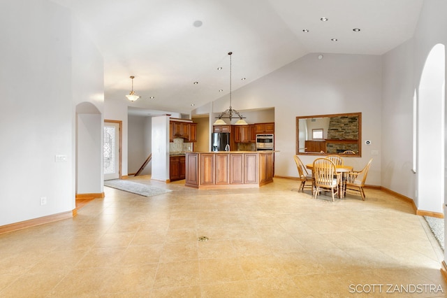 kitchen featuring stainless steel fridge with ice dispenser, brown cabinets, hanging light fixtures, light countertops, and high vaulted ceiling