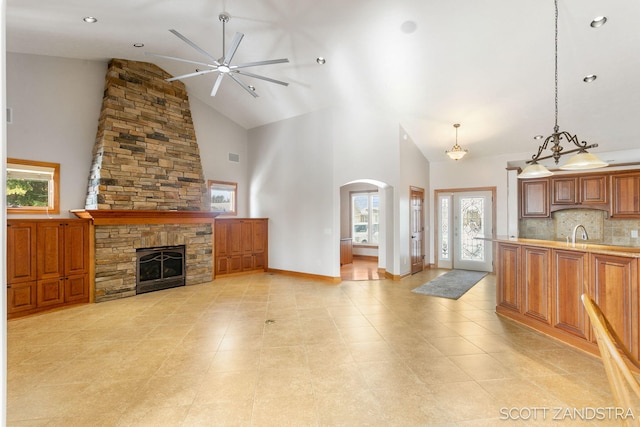 living room featuring arched walkways, a fireplace, a ceiling fan, high vaulted ceiling, and baseboards