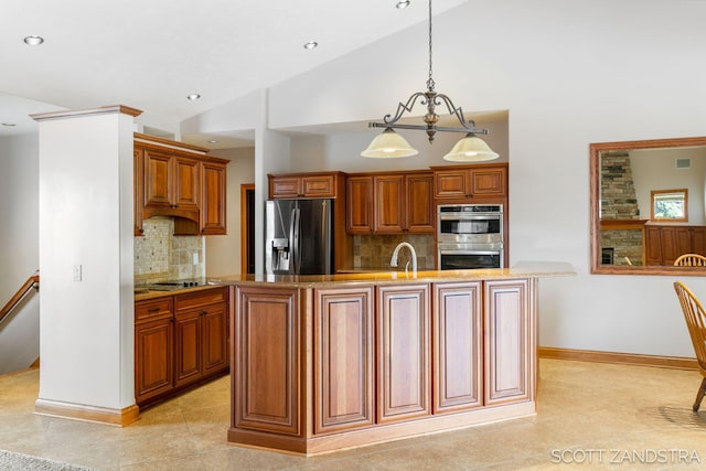 kitchen with a center island with sink, brown cabinets, hanging light fixtures, stainless steel appliances, and a sink