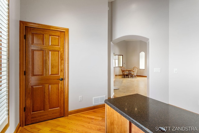 corridor with arched walkways, light wood-type flooring, visible vents, and baseboards