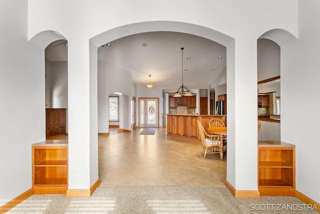 interior space featuring brown cabinetry, decorative backsplash, light colored carpet, freestanding refrigerator, and decorative light fixtures