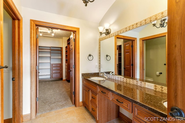 bathroom with double vanity, lofted ceiling, toilet, tile patterned flooring, and a sink