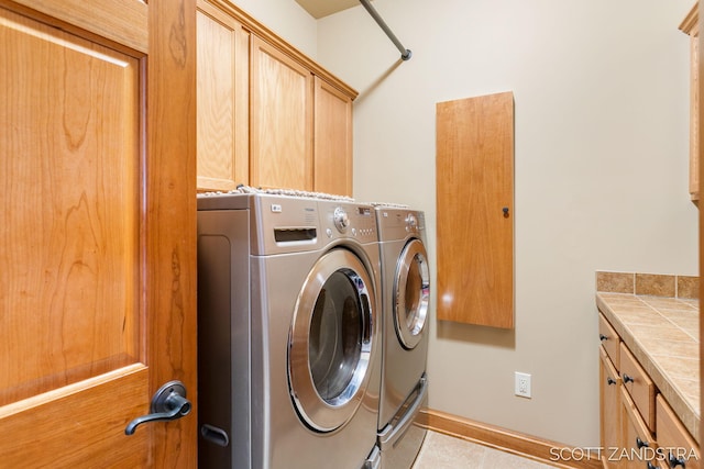 clothes washing area with cabinet space, light tile patterned floors, and washer and dryer