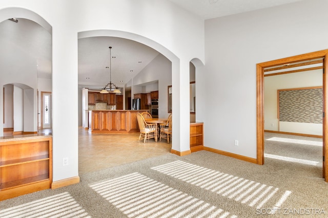 living area with light carpet, high vaulted ceiling, arched walkways, and baseboards