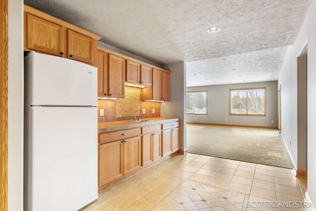 kitchen with light tile patterned floors, a sink, light countertops, freestanding refrigerator, and decorative backsplash