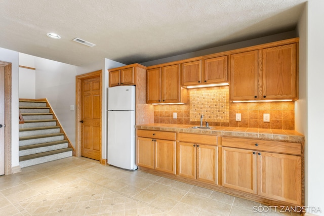 kitchen with tile countertops, tasteful backsplash, visible vents, freestanding refrigerator, and a sink