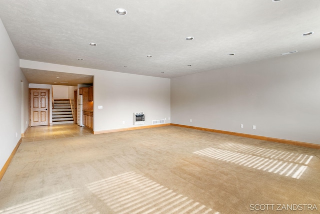 unfurnished living room with baseboards, stairway, visible vents, and light colored carpet