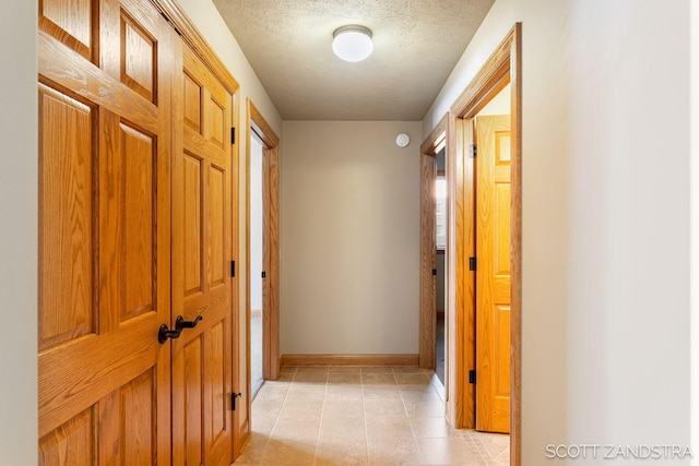 hall featuring a textured ceiling, light tile patterned floors, and baseboards