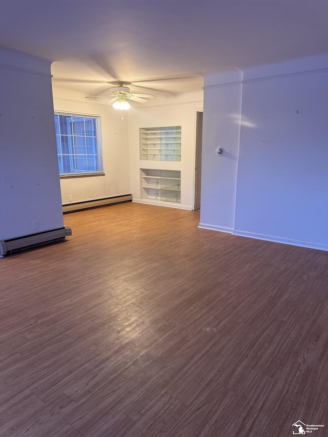 empty room with built in shelves, baseboard heating, a ceiling fan, wood finished floors, and baseboards