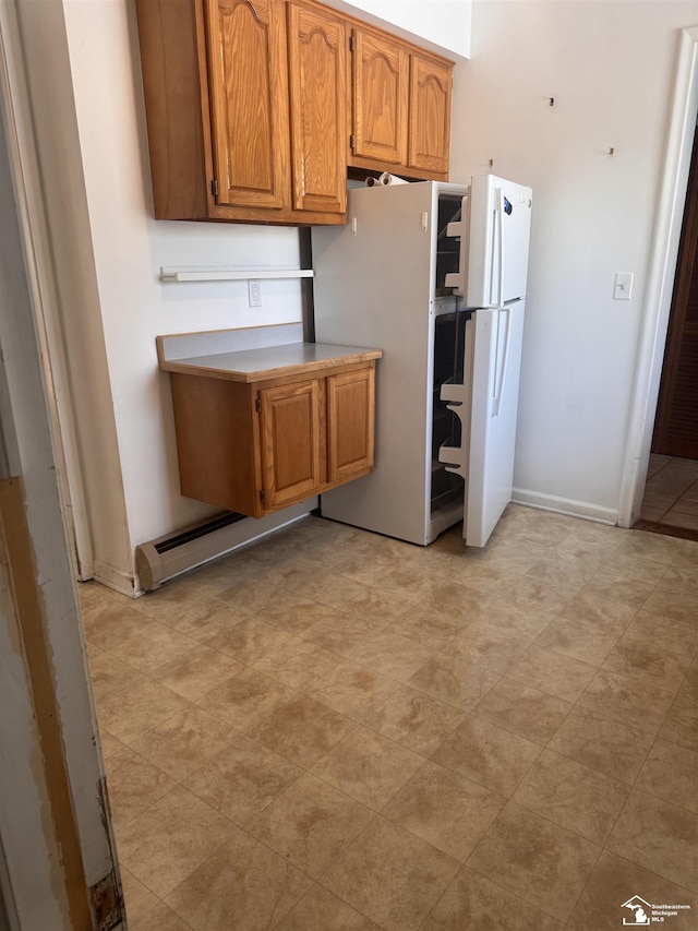 kitchen featuring brown cabinetry, baseboards, light countertops, and freestanding refrigerator