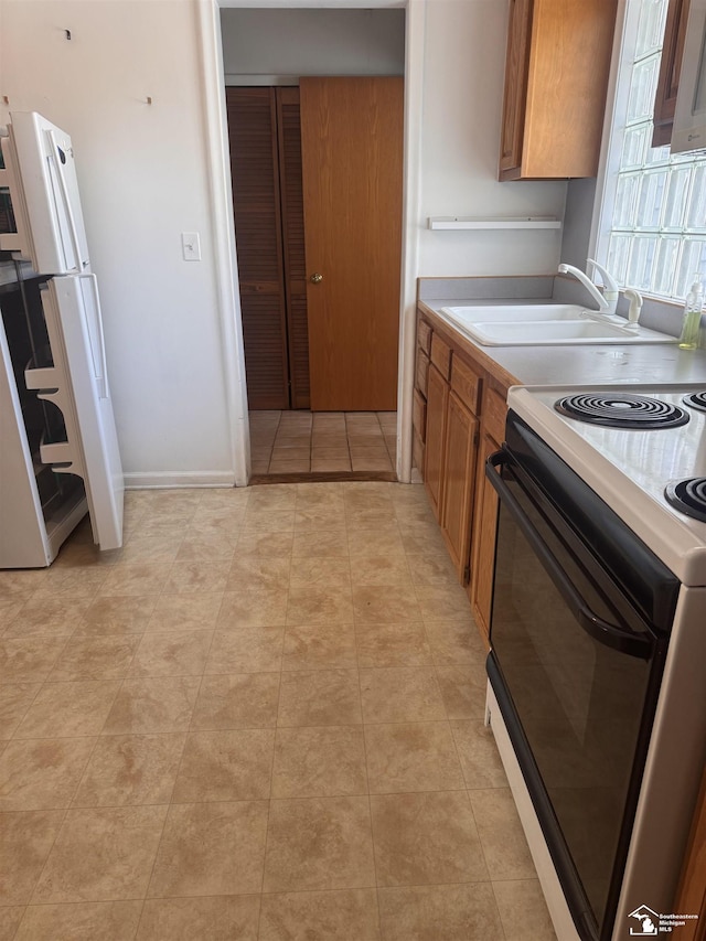 kitchen with black electric range, brown cabinets, light countertops, freestanding refrigerator, and a sink