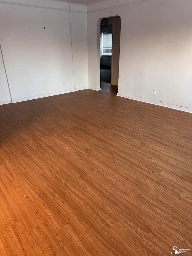 empty room with arched walkways and dark wood-type flooring