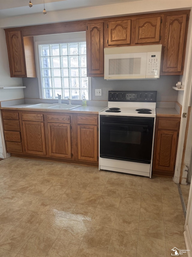 kitchen with electric stove, brown cabinets, light countertops, white microwave, and a sink