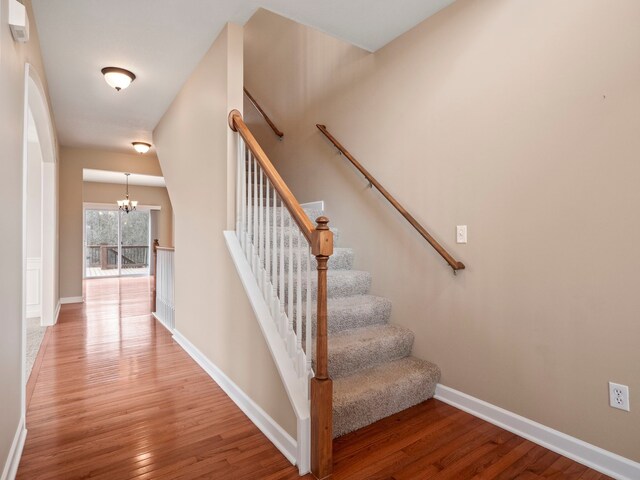 staircase featuring a notable chandelier, wood finished floors, and baseboards