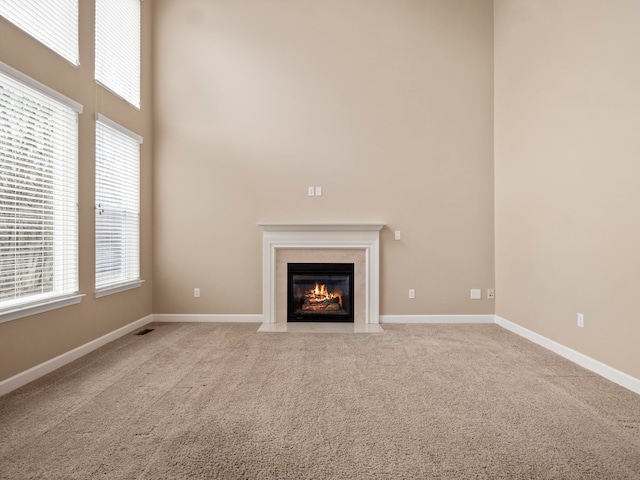 unfurnished living room featuring visible vents, baseboards, a fireplace with flush hearth, carpet flooring, and a high ceiling