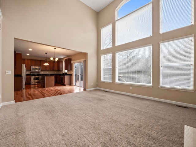 unfurnished living room with a high ceiling, baseboards, visible vents, and light carpet