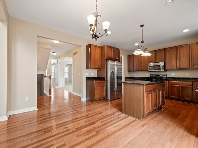 kitchen with light wood finished floors, visible vents, decorative light fixtures, arched walkways, and stainless steel appliances