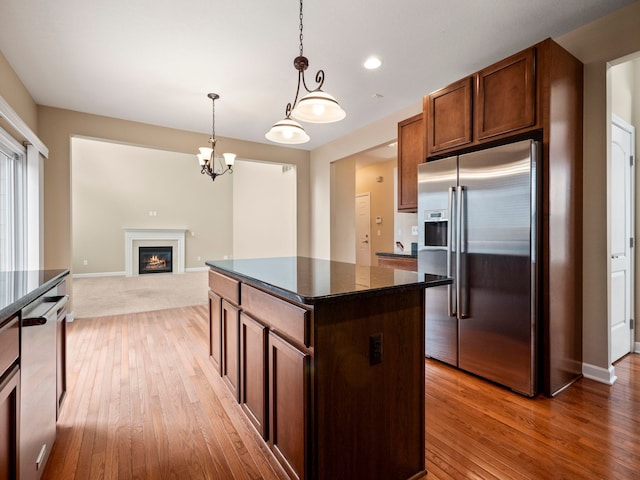 kitchen with light wood finished floors, a center island, pendant lighting, a glass covered fireplace, and stainless steel appliances