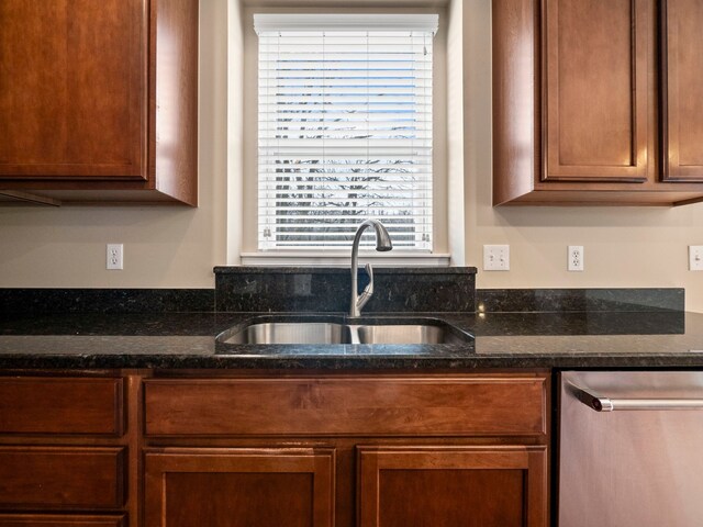 kitchen featuring dishwasher, dark stone counters, brown cabinetry, and a sink