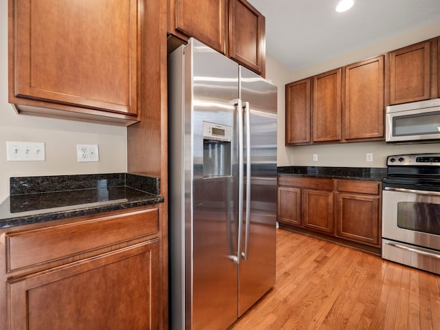 kitchen with dark stone countertops, brown cabinetry, light wood-type flooring, and stainless steel appliances