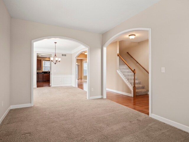 empty room featuring visible vents, stairway, arched walkways, carpet, and an inviting chandelier