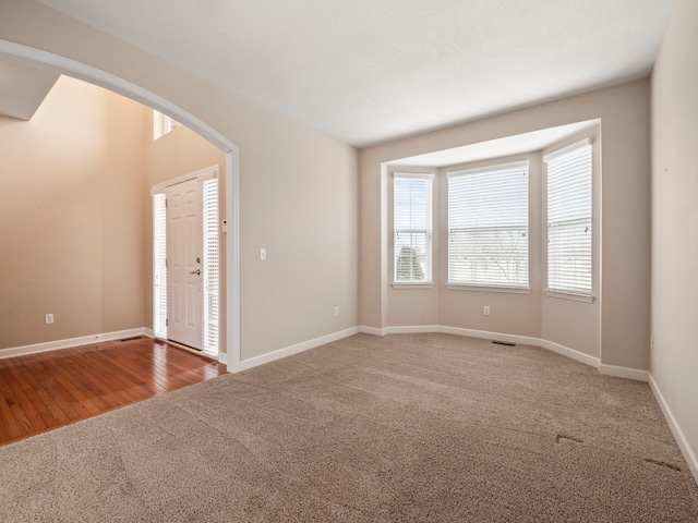 empty room with arched walkways, visible vents, baseboards, and carpet floors