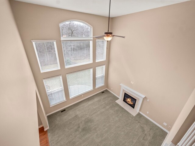 unfurnished living room with visible vents, a fireplace with flush hearth, carpet, baseboards, and ceiling fan