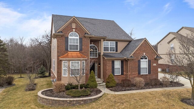 traditional-style home with brick siding, a front lawn, and roof with shingles