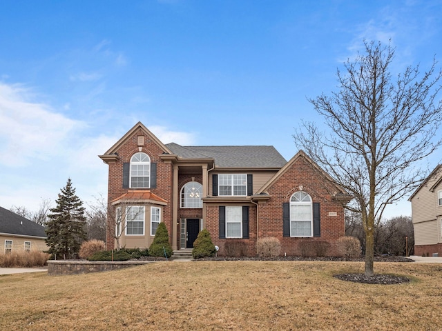 traditional home featuring a front yard, brick siding, and a shingled roof