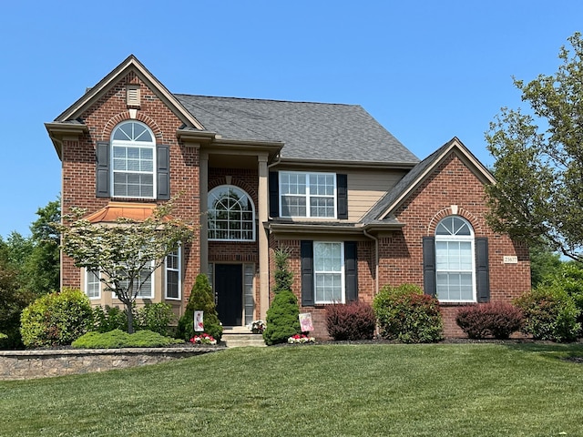 traditional home with brick siding, a shingled roof, and a front yard