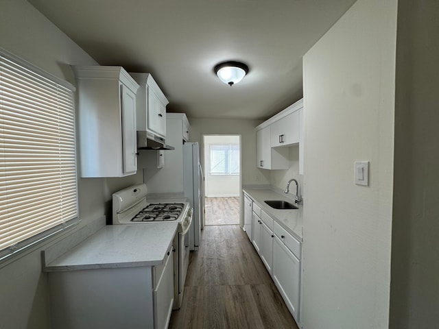 kitchen featuring white gas stove, under cabinet range hood, a sink, white cabinetry, and light countertops