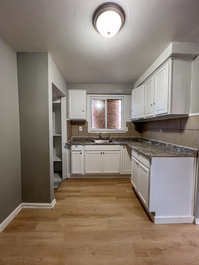 kitchen with a textured ceiling, a sink, white cabinetry, baseboards, and light wood-type flooring