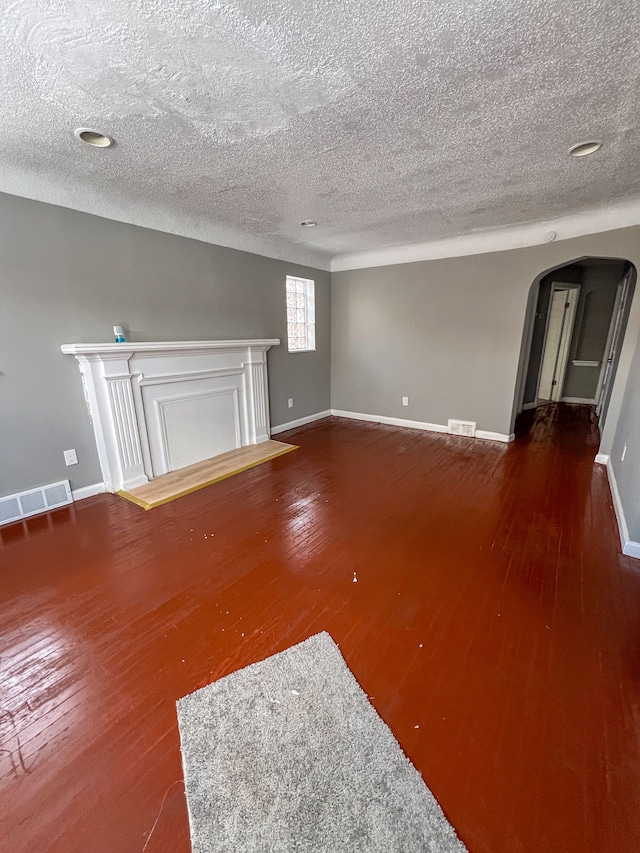 unfurnished living room with arched walkways, baseboards, visible vents, and hardwood / wood-style floors