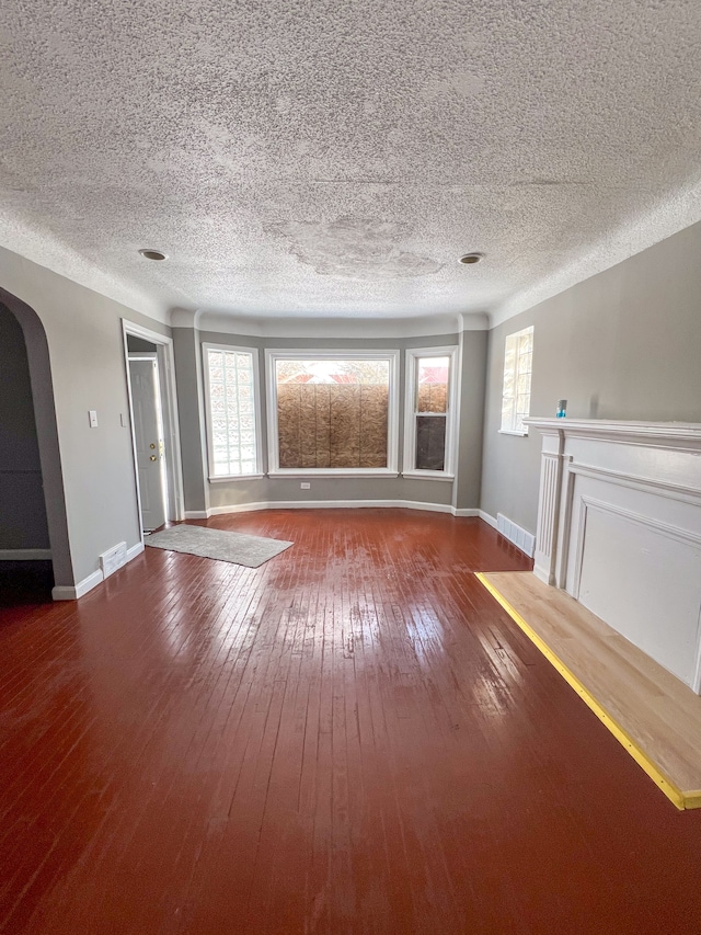 unfurnished living room with arched walkways, dark wood-type flooring, visible vents, and a healthy amount of sunlight