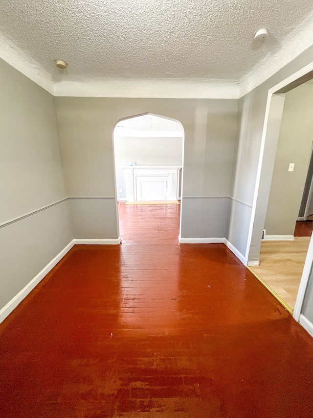 unfurnished room featuring arched walkways, a textured ceiling, wood finished floors, and baseboards