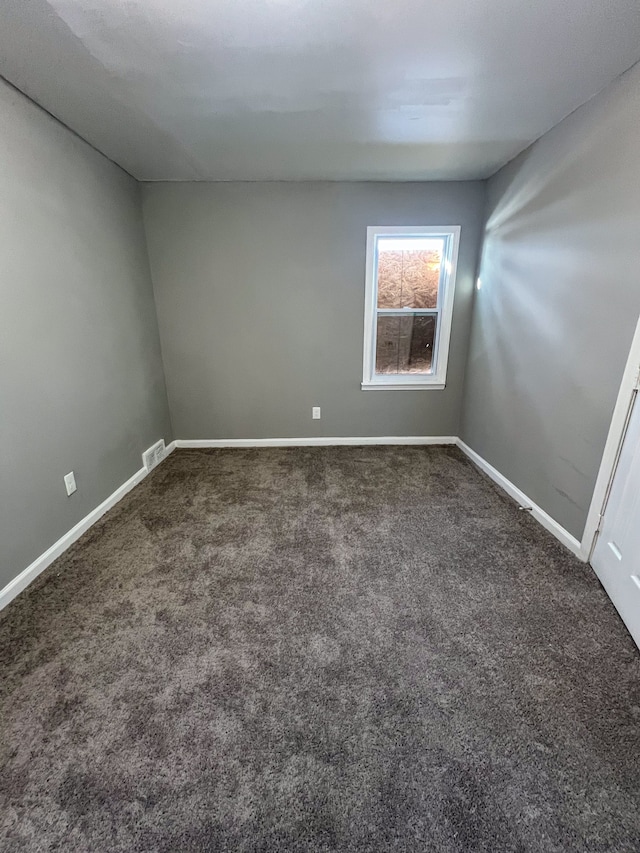 empty room featuring dark carpet, visible vents, and baseboards