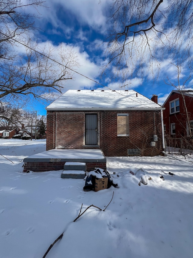 snow covered back of property with brick siding