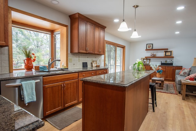 kitchen featuring a sink, stainless steel dishwasher, light wood-type flooring, decorative backsplash, and dark stone counters