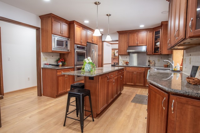 kitchen featuring brown cabinets, under cabinet range hood, stainless steel appliances, and a sink