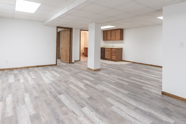 finished below grade area with a paneled ceiling, a sink, light wood-style flooring, and baseboards