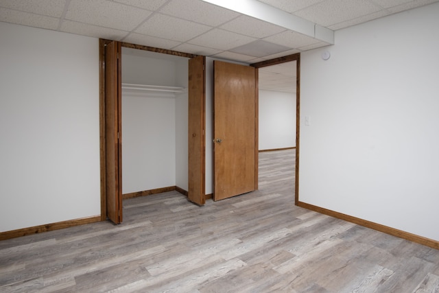 unfurnished bedroom featuring a paneled ceiling, light wood finished floors, baseboards, and a closet