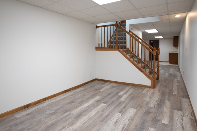 unfurnished room with stairs, a drop ceiling, baseboards, and wood finished floors