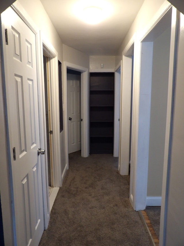 hall featuring dark colored carpet and baseboards